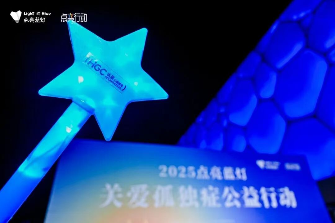A blue star-shaped light bearing the HGC Foundation mark in front of Beijing's illuminated Water Cube